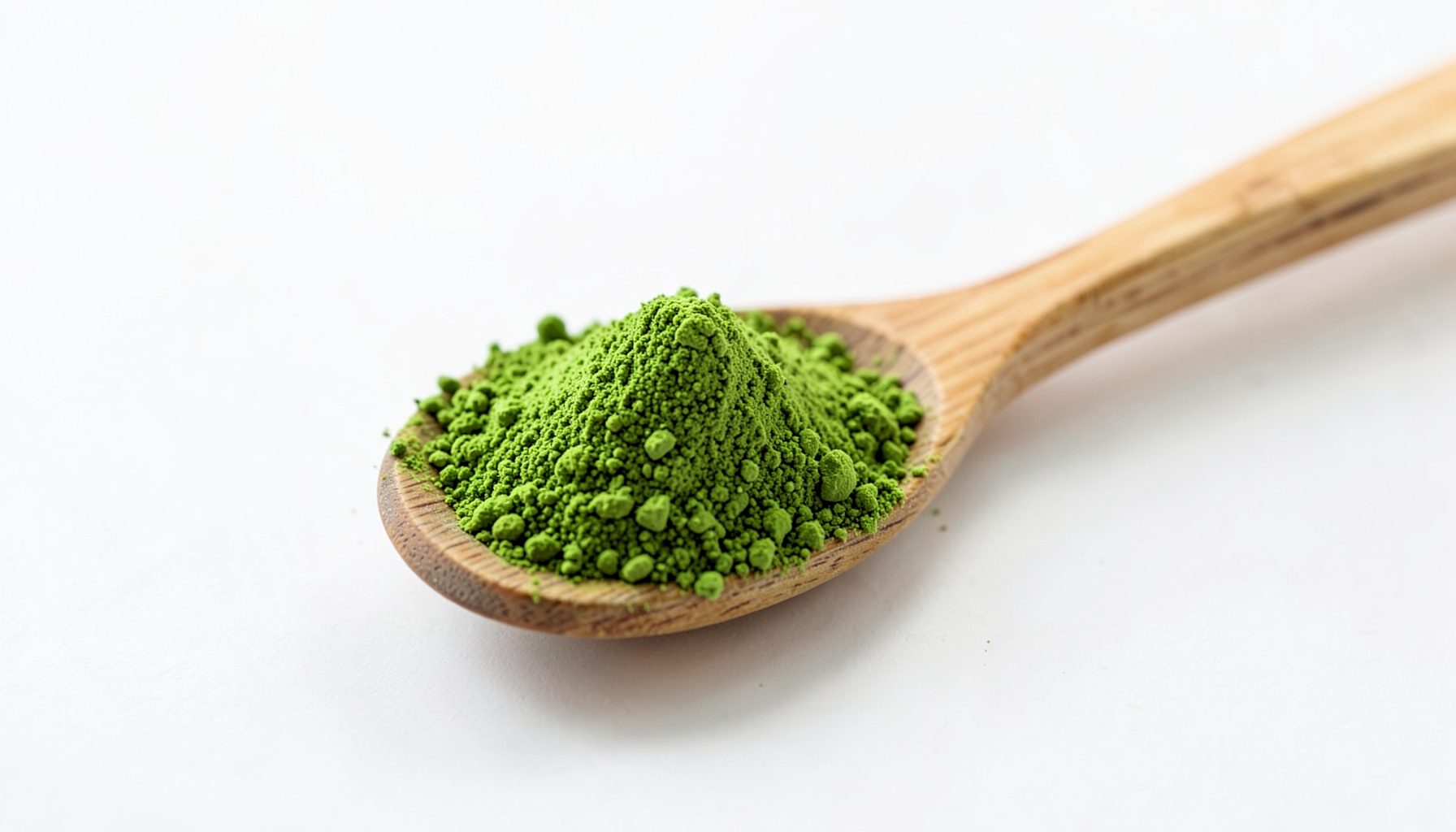 Poudre de matcha vert vif dans une cuillère en bambou sur fond clair.